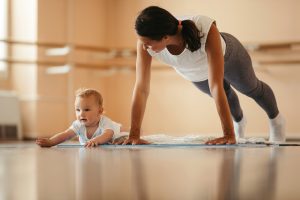 a Young mother exercising push-ups while being on sports training with her baby. baby essential exercise.