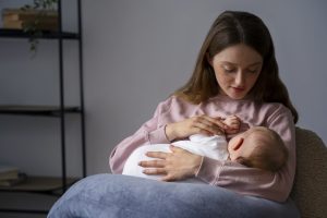 Demand or fexible feed baby? a young mother with a pink jumper on looking down at her baby while she breastfeeds