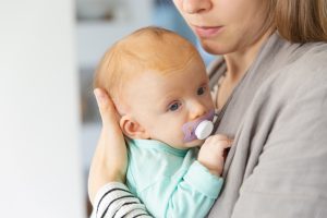 Closeup of cute adorable red haired baby with a dummy in mothers arms. Portrait of young woman and cute little child in home interior. Happy new mum concept Image by pch.vector on Freepik